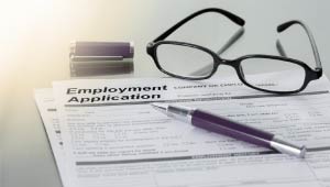 A picture of an employment application on top of a white surface. On top of the application are glasses, and a pen.